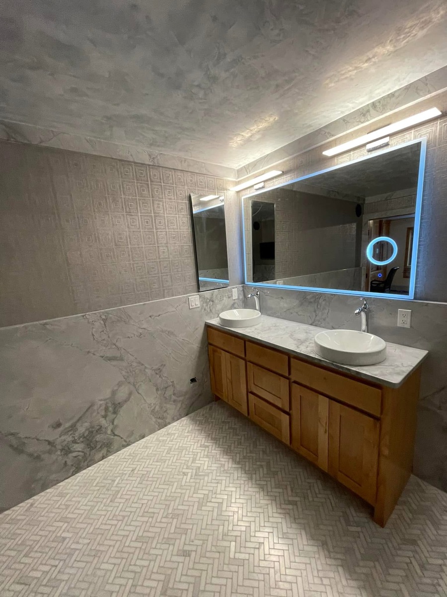 Marble double vanity with backlit LED mirror and full marble-slab shower with bench and dual showerheads, installed by Precision Granite & Marble.