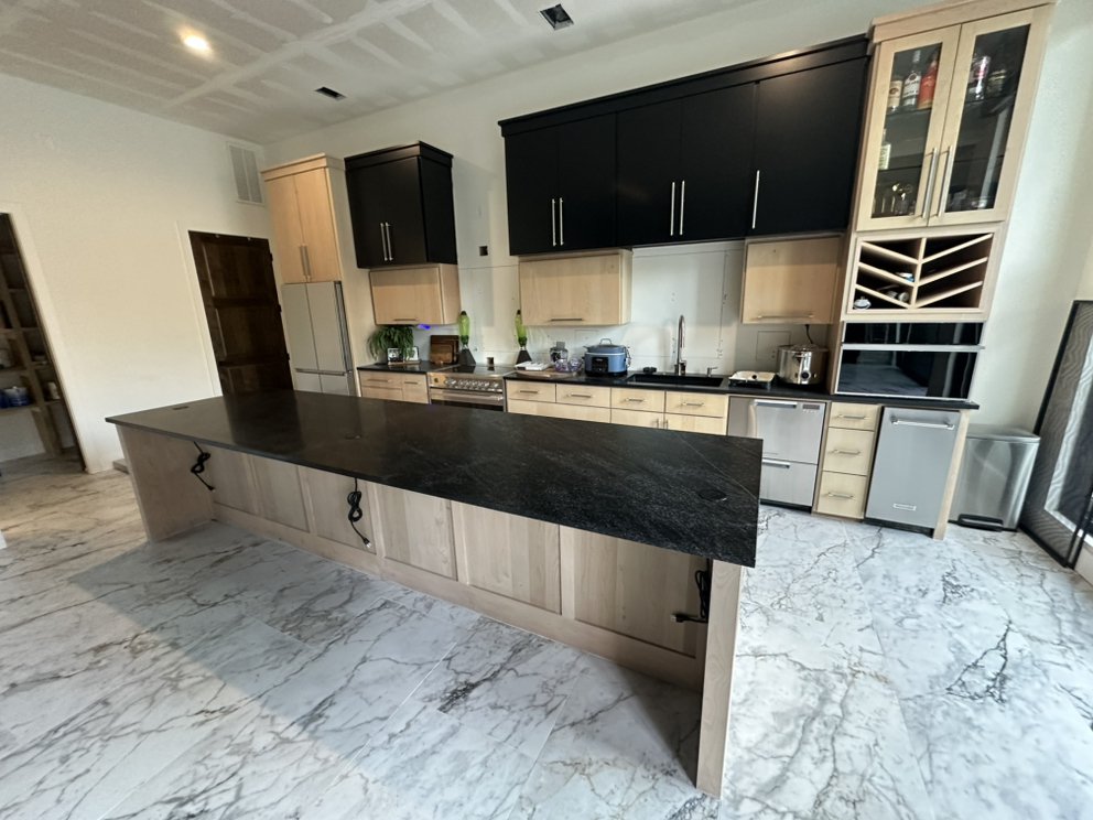 Leathered black granite island alongside custom wine cabinetry — a real Precision Granite & Marble project.
